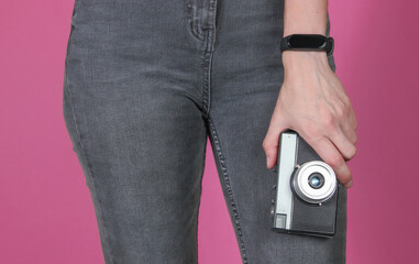 Woman in jeans holds a retro film camera on pink background. Crop photo
