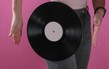 Woman in jeans with vinyl record on pink background. Crop photo