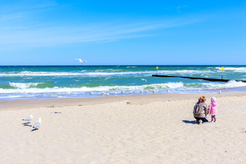 Unidentified woman with small child feeding seagulls on beautiful white sand beach in Kolobrzeg, Baltic Sea coast, Poland