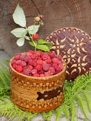 Beautiful raspberries in folk dishes on green grass and woody background. Summer berry harvest composition