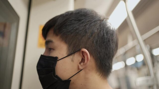 Asian male wearing black mask look at camera then look out the window, standing next to train door. covid-19 pandemic disease, public transport, after tiring day at work, new normal life rush hour