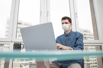 A guy in a protective face mask works at a computer from home during a virus epidemic. Quarantine during viral infection