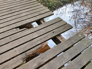 Old damaged broken wooden park bridge with water under the bridge