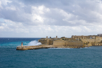 VALLETTA, MALTA - DEC 31st, 2019: View from Fort St Elmo on to the Ricasoli Grand Harbour East Breakwater and red lighthouse during strong waves