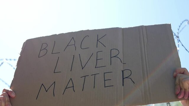 Poster BLACK LIVES MATTER in hands. Stop racism against the blue sky. Stop racism concept.
