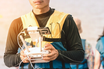 Young man in blue and yellow life vest controlling a drone to take pictures of ocean coast with tourists while traveling on a raft in the sea. Hands holding drone remote controller.