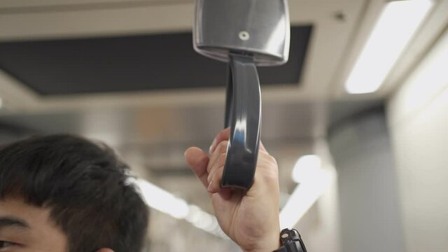 close up Asian young man with hand grab on subway train handle, wear black protective mask, standing in subway train, new normal risk of public transport, virus bacteria spreading surface, urban lfie