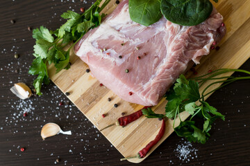 greens, seasonings and meat on a cutting board. a piece of pork, pepper, garlic, salt. Cook at home. fresh food