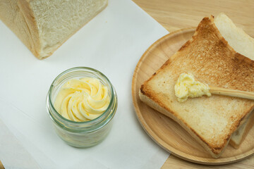 Tosted bread with butter cup and bread loaf on wood plate