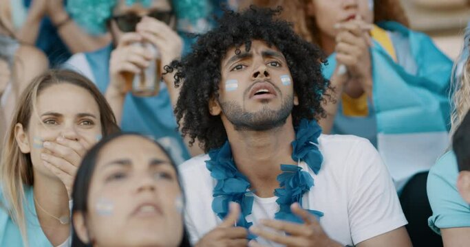Sports fans in crowd expressing disappointment during game. Anxious Argentinian soccer fans in disappointment while watching a live match in stadium.
