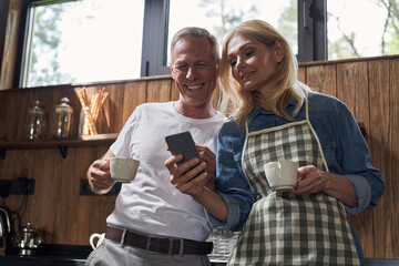 Happy couple drinking coffee and using smartphone