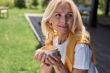 Jolly mature woman with hot drink outdoors