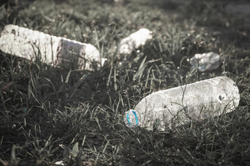 Garbage from plastic water bottle that are thrown away on the grass field in park which is a problem and pollution to the environment with dark black and white tone (monochrome) close-up.