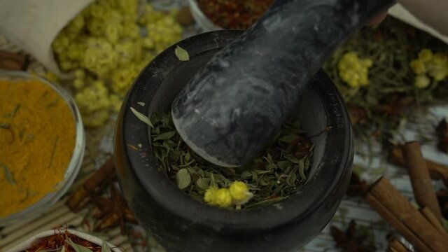 Woman's hand mixes and crushes dried flowers by granite mortar with pestle in slow motion. Healthy and organic food, herb medicine, natural care, aromatherapy and organic cosmetics concept.