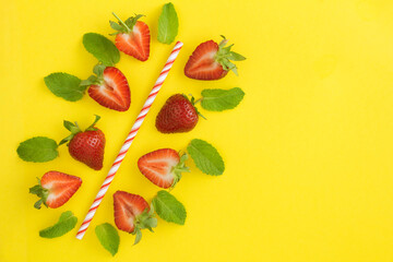 Composition with a cocktail straw, strawberries and mint  on the yellow background. Top view. Copy space.