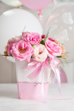 bouquet of delicate pink roses and eustomas in a box on a background of balloons. happy birthday concept. vertical image. close-up.