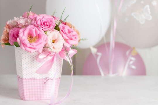 beautiful bouquet of pastel roses and eustomas in a box with a ribbon on a background of balloons. birthday party concept. place for text. horizontal image.