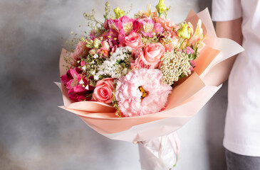 woman in a white t-shirt holding a big beautiful bouquet of rose, eustoma, alstroemeria flowers on a gray background. Floral shop concept. Flowers delivery. copy space.