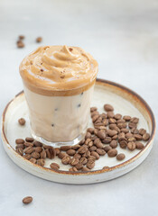 close-up of a glass with Dalgona frothy coffee with ice on a light background. drink trend. vertical image. copy space