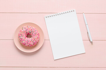 Notebook, pen and donut on a pink wooden background