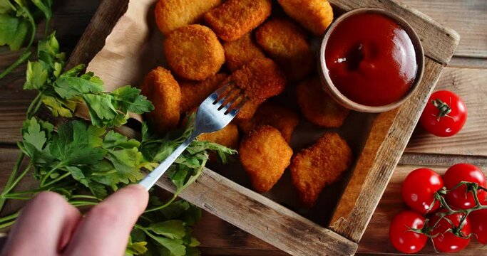 Male hand with a fork dips nuggets in the sauce.