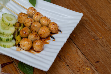 Meatballs toasted on wood dish and a sauce decorated with coriander placed on the table brown wood. Grill pork balls pour at street food market of Thailand ,on top view