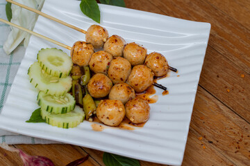 Meatballs toasted on wood dish and a sauce decorated with coriander placed on the table brown wood. Grill pork balls pour at street food market of Thailand ,on top view