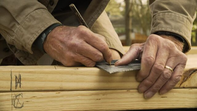 Older Male Construction Worker Marks Wood with Speed Square, Close Up