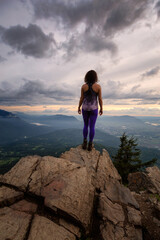 Fototapeta premium Adventurous Girl on top of a Rocky Mountain overlooking the beautiful Canadian Nature Landscape during a dramatic Sunset. Taken in Chilliwack, East of Vancouver, British Columbia, Canada.