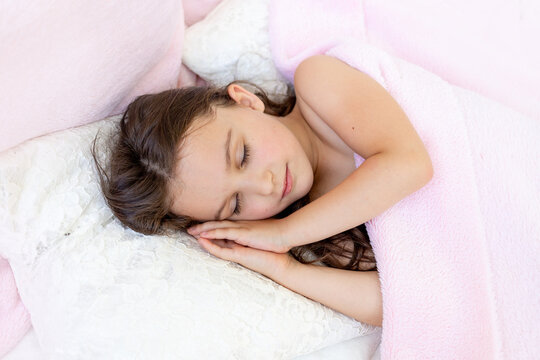 a little girl of 5-6 years old smiles in her sleep, the child lies in bed with her hands folded under her head