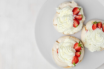 Top view of three Pavlova meringue cakes with fresh strawberry on a white plate on white background with copy space. Homemade pastry.