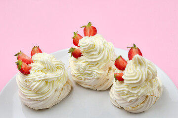 Meringue cakes with strawberry and whipped cream on a plate on a pink background with copy space.