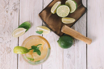 Top view of mojito cocktail with ice, lime wedges and mint leafs on a wooden board with chopped limes. Cocktail concept.