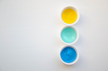 Three cups with yellow, mint and blue acrylic paint on the white background