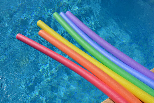 Rainbow coloured pool noodles floating in a swimming pool on a bright and sunny day