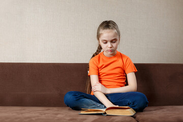 Child girl reading a book relaxing on a couch. Kids read books at home. Children learning and doing homework after school. Charming child on a sofa.