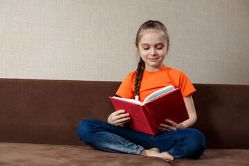 Kid Girl is Reading a Book on the couch at home