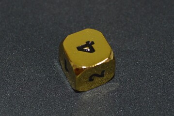 Gold metallic d6 six sided dice on foam surface in bright sunshine