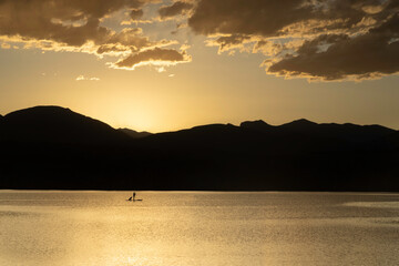 A Silhouette Paddleboarder with their dog on a mountain lake at sunset
