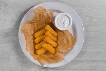 Flat lay of fried and roast cheese bites on the light color plate with sauce on the wooden background.