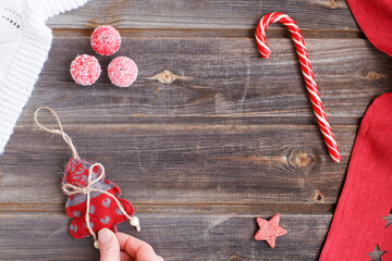 New year flat lay: Christmas linen tree with hearts in fingers of the hand, candy cane, tiny snow sugar apples, white woolen plaid and red tablecloth with stars on a rustic wooden background
