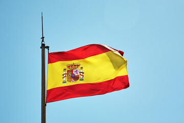 Spanish flag flying on a flagpole on sky background.