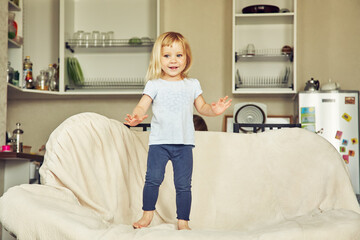 funny little girl standing on a couch. child playing at home. - 359257609