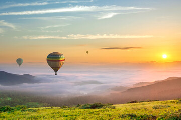 Big hot air baloons over idyllic landscape with green grass covered morning mountains with distant...