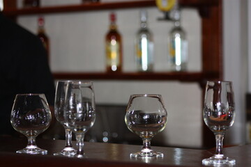 Wine glasses and drinking glasses on the counter at a bar with bottles blurred out in the back.  