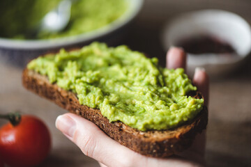 Toast with mashed avocado. Hand holding avocado rye bread toast. Healthy vegan vegetarian food