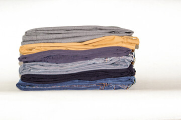 Jeans of different colors lie in a stack on a white surface. They are black, brown, blue and yellow...