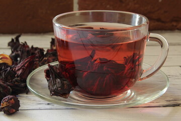 Red hot hibiscus tea in a glass mug on a wooden table among dry tea custard. Red tea karkade. 