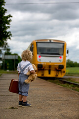 Sweet toddler child with teddy bear, book and vintage suitcase waiting for the train on a train station