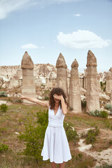 Young woman in dress expressing emotion while posing in front of high stone pillars in Cappadocia, Turkey
